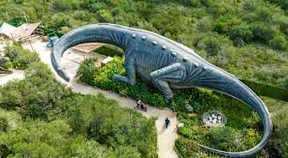 Suuri dinosauruspatsas viheralueen ympäröimänä, näkymä ylhäältä. (Tekoälyn luoma teksti)