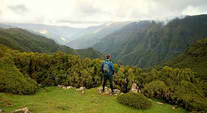 Henkilö seisoo vihreällä kukkulalla ja katsoo metsän peittämiä vuoria. (Tekoälyn luoma teksti)