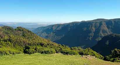 Kuvassa näkyy maisema, jossa on vehreitä mäkiä ja vuoria kirkkaan sinisen taivaan alla. (Tekoälyn luoma teksti)