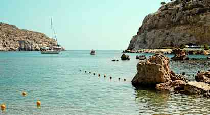 Lahti, jossa on kirkasta vettä ja kivinen rannikko, taustalla näkyy vene ja pienempi alus. (Tekoälyn luoma teksti)