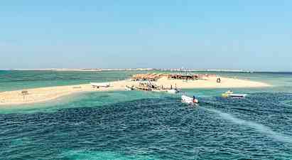 Pieni hiekkasaari, jossa on veneitä laiturilla, kirkkaan sinisen veden ympäröimänä. (Tekoälyn luoma teksti)