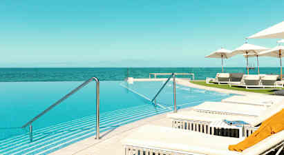 Ikkunaton uima-allas, josta on näkymä merelle, ympärillä aurinkotuoleja ja aurinkovarjoja. (Tekoälyn luoma teksti)