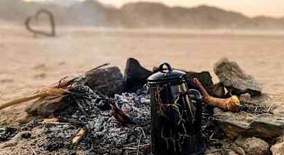 Kahvikannu seisoo sammuneen nuotion vieressä autiomaan maisemassa. (Tekoälyn luoma teksti)