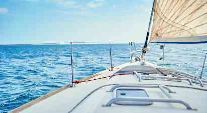 Lähikuva purjeveneen keulakannesta, valkoinen purje ja sininen meri taustalla. (Tekoälyn luoma teksti)