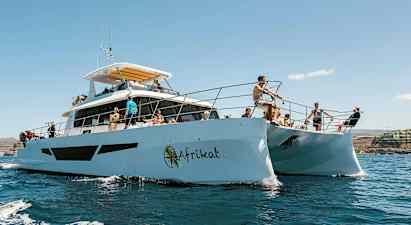 Henkilöitä katamaraanilla aurinkoisessa säässä, ympärillään vettä ja taustalla rantaviiva. (Tekoälyn luoma teksti)