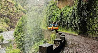 Kelta-oranssi jeep kahden hengen joukolla tiellä vesiputouksen kupeessa vihreässä laaksossa. (Tekoälyn luoma teksti)