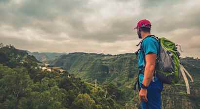 Reppu selässään oleva henkilö katselee vihreää laaksoa pilvisellä säällä. (Tekoälyn luoma teksti)