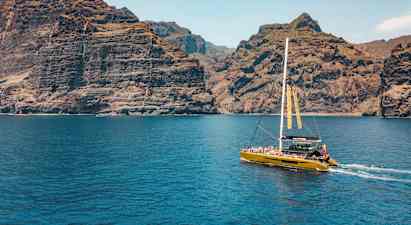 Katamaraani purjehtii lähellä korkeita kallioita, kirkkaan sininen vesi etualalla. (Tekoälyn luoma teksti)