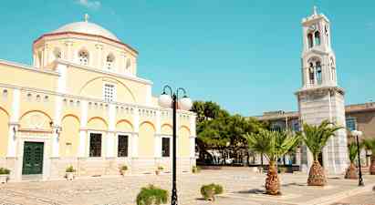 Keltainen rakennus, jossa on kupoli ja kellotorni, sekä palmuja ja katuvalaisin. (Tekoälyn luoma teksti)