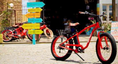 Punainen polkupyörä mukulakivipinnalla, taustalla värikkäitä tienviittoja. (Tekoälyn luoma teksti)