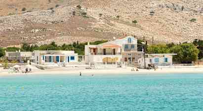 Kuva kirkkaan sinisestä merenlahdesta, jossa on hiekkaranta sekä taloja ja kukkuloita taustalla. (Tekoälyn luoma teksti)