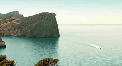 Kallio rannikon äärellä, jossa vene ajaa vedessä. (Tekoälyn luoma teksti)