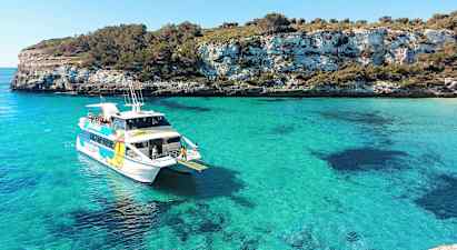 Valkoinen vene matkustajineen turkoosinsinisessä lahdessa, jota ympäröivät kalliot ja vehreys. (Tekoälyn luoma teksti)