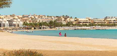 Ranta, taustalla rakennuksia ja palmuja. (Tekoälyn luoma teksti)