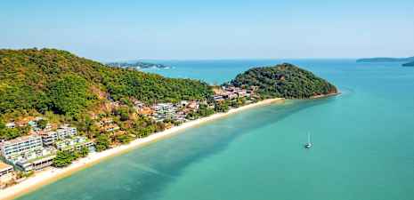 Ilmakuva rannasta, jossa kirkas sininen vesi, ympärillä vehreitä kukkuloita ja lomakeskuksia. (Tekoälyn luoma teksti)