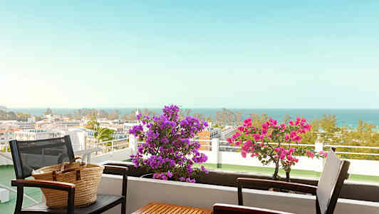 Parveke, jossa pöytä ja tuolit, kukkia ja merinäköala. (Tekoälyn luoma teksti)