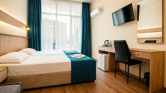 Hotellihuone, jossa on parivuode, työpöytä, tuoli, seinälle asennettu televisio ja suuret ikkunat tummansinisillä verhoilla. (Tekoälyn luoma teksti)