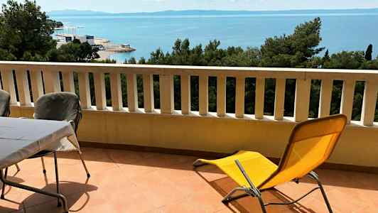 Parveke, jossa pöytä, tuoleja ja aurinkotuoli sekä näkymä merelle. (Tekoälyn luoma teksti)