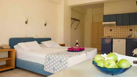 Huoneessa on sänky, jossa on sininen sängynpääty, keittiö ja pöytä hedelmillä. (Tekoälyn luoma teksti)