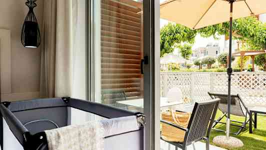 Kuva huoneesta, jossa on pinnasänky lähellä lasi-ikkunaa, joka avautuu terassille, jossa on ulkokalusteita ja varjo. (Tekoälyn luoma teksti)