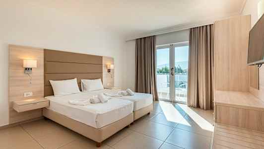 Valoisa hotellihuone, jossa kaksi vuodetta, parvekkeen ovi ja puuhuonekalut. (Tekoälyn luoma teksti)