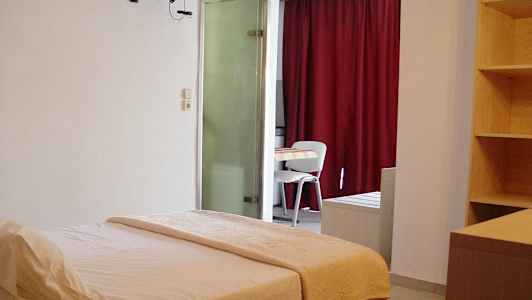 Hotellihuone, jossa on sänky, pöytä ja tuolit sekä hylly ja punaiset verhot. (Tekoälyn luoma teksti)
