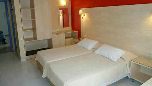 Hotellihuone, jossa on kaksi vierekkäistä yhden hengen sänkyä, vaatekaappi ja peilipöytä. (Tekoälyn luoma teksti)