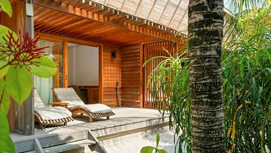 Puisella terassilla aurinkotuoleja ja ympärillä vehreyttä puisen rakennuksen vieressä. (Tekoälyn luoma teksti)