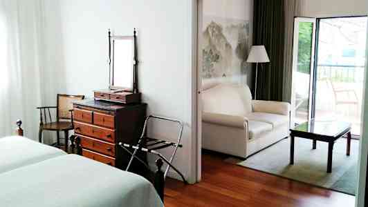 Hotellihuone, jossa on kaksi sänkyä, lipasto peilillä ja avoin oleskelutila sohvalla ja pöydällä. (Tekoälyn luoma teksti)