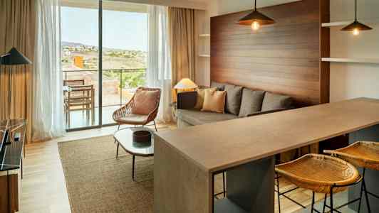 Moderni olohuone, jossa on sohva, nojatuoli ja keittiöbaari. Suuret ikkunat avautuvat terassille. (Tekoälyn luoma teksti)