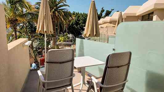 Kaksi tuolia ja pöytä terassilla, näkymä palmupuihin ja rakennuksiin. (Tekoälyn luoma teksti)