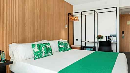 Hotellihuone, jossa parivuode, vihreät koristetyynyt ja puupaneelikuvio seinässä. (Tekoälyn luoma teksti)