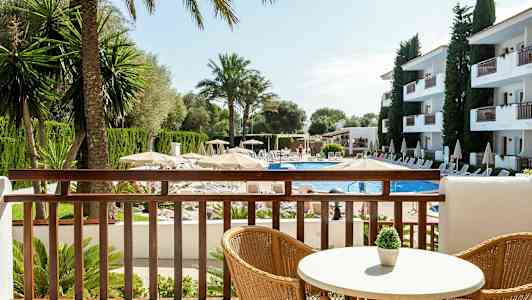 Näkymä parvekkeelta altaalle, jonka ympärillä on aurinkotuoleja, aurinkovarjoja ja rakennuksia. (Tekoälyn luoma teksti)