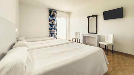 Hotellihuone, jossa on kolme yhden hengen sänkyä, työpöytä peilillä, kaksi tuolia ja seinään kiinnitetty televisio. (Tekoälyn luoma teksti)