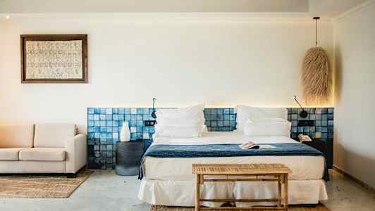 Tyylikäs hotellihuone, jossa on parivuode, sininen sängynpääty, oleskelualue ja vaaleita koristeellisia elementtejä. (Tekoälyn luoma teksti)