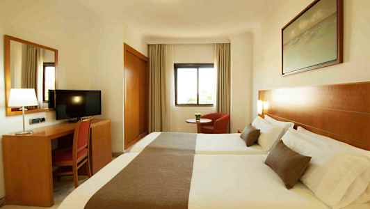 Hotellihuone, jossa on kaksi sänkyä, kirjoituspöytä tuolin ja television kanssa sekä ikkuna ja nojatuoli. (Tekoälyn luoma teksti)