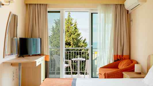 Hotellihuone, jossa parveke, sänky, nojatuoli ja televisio. (Tekoälyn luoma teksti)