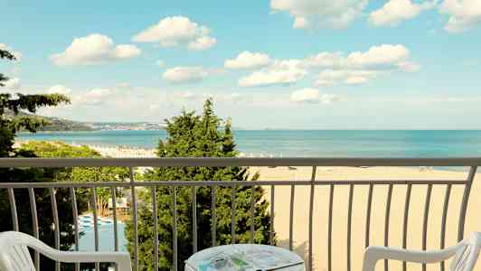 Näkymä parvekkeelta rannalle ja merelle, edessä tuolit ja pöytä. (Tekoälyn luoma teksti)