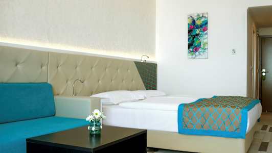 Moderni hotellihuone, jossa on parivuode, turkoosi sohva ja seinätaide. (Tekoälyn luoma teksti)