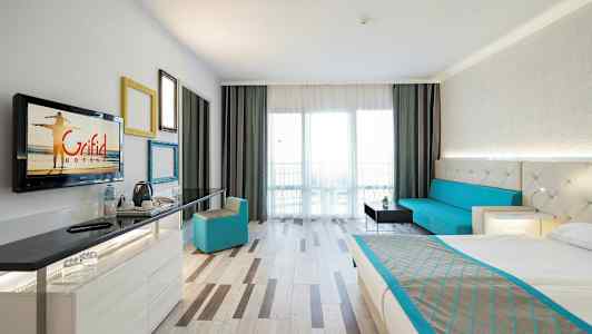 Hotellihuone, jossa on sänky, istuinryhmä, työpöytä ja parveke. (Tekoälyn luoma teksti)