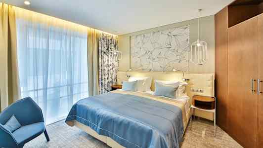 Hotellihuone, jossa on parivuode, sininen päiväpeite ja koristeellinen seinä sängyn takana. (Tekoälyn luoma teksti)