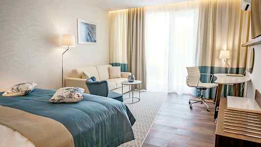 Hotellihuone, jossa sänky, sohva, pöytä ja kirjoituspöytä tuoleineen. (Tekoälyn luoma teksti)