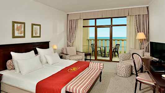 Hotellihuone, jossa parivuode, oleskelutila, kirjoituspöytä ja parveke merinäköalalla. (Tekoälyn luoma teksti)