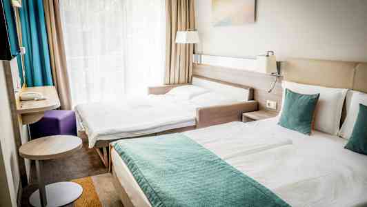 Kaksi sänkyä hotellihuoneessa, jossa suuri ikkunaseinä ja verhot. (Tekoälyn luoma teksti)