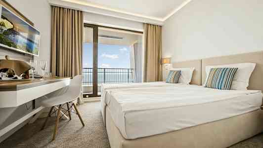 Hotellihuone, jossa kaksi sänkyä, kirjoituspöytä ja parveke merinäköalalla. (Tekoälyn luoma teksti)