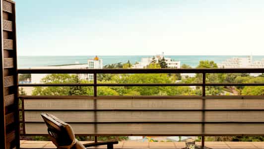 Näkymä parvekkeelta yli vehreyden, rakennusten ja meren. (Tekoälyn luoma teksti)