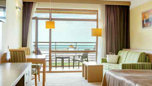 Hotellihuone, jossa istuma-alue, pöytä, sänky ja parveke näkymällä. (Tekoälyn luoma teksti)