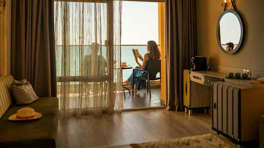 Hotellihuone, jossa parveke, ja henkilö lukemassa merinäköalalla. (Tekoälyn luoma teksti)