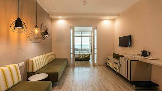 Hotellihuone, jossa on istuinpenkki, pöytä, televisio ja sänky taustalla. (Tekoälyn luoma teksti)