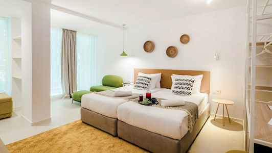 Moderni hotellihuone, jossa kaksi erillistä vuodetta, vihreä istuin ja koristeita seinällä. (Tekoälyn luoma teksti)